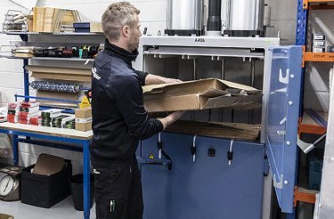 Auto mechanic loads cardboard into a baler