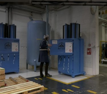 man in manufacturing environment opening a blue baler with Mil-tek logo