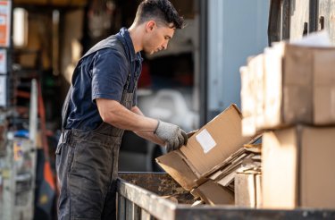 man putting cardboard box in container